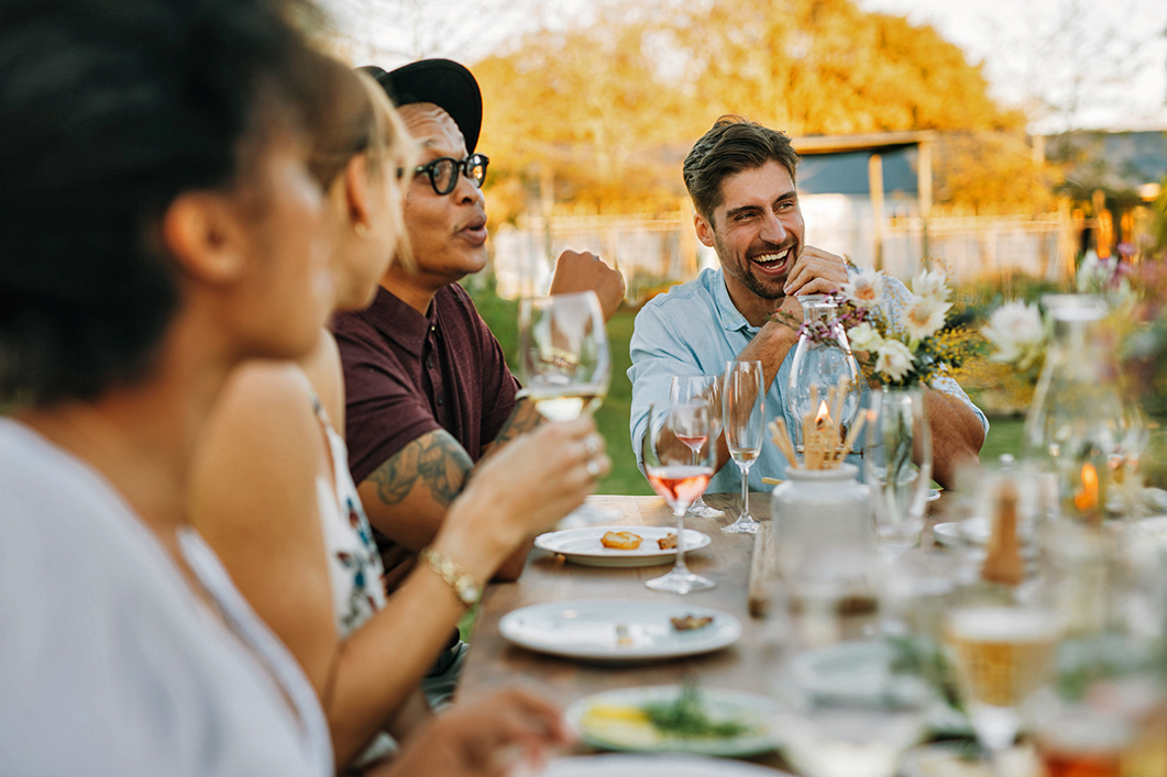 <p>A lifestyle photo showing a diverse group of people enjoying a meal and wine in an outdoor setting. </p>
